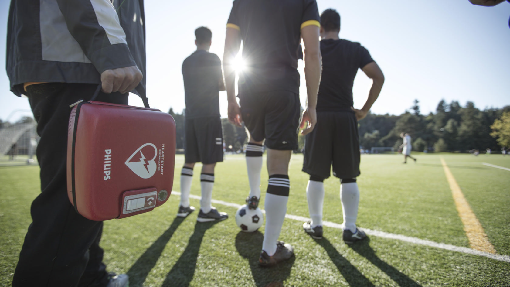 A youth soccer coach carrying a HeartStart AED onto the field